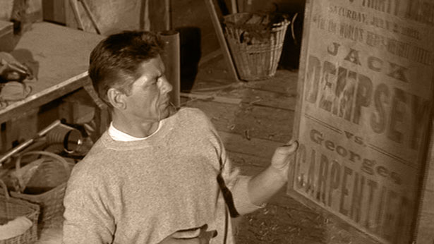 Lew (Charles Bronson) holds up an old poster found advertising 1921's Dempsey vs. Carpentier fight in 1962's KID GALAHAD (United Artists)